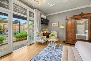 A room with a large sliding glass door leading to an outdoor area, a white sofa, a patterned rug, a wooden cabinet, and a television mounted on the wall.