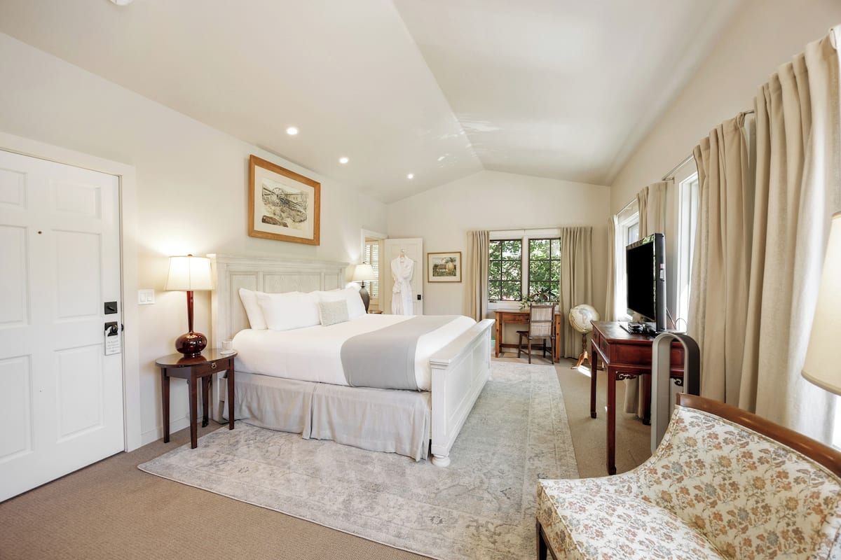 A hotel room with a large bed, a desk with a chair, a television, and a window with curtains.