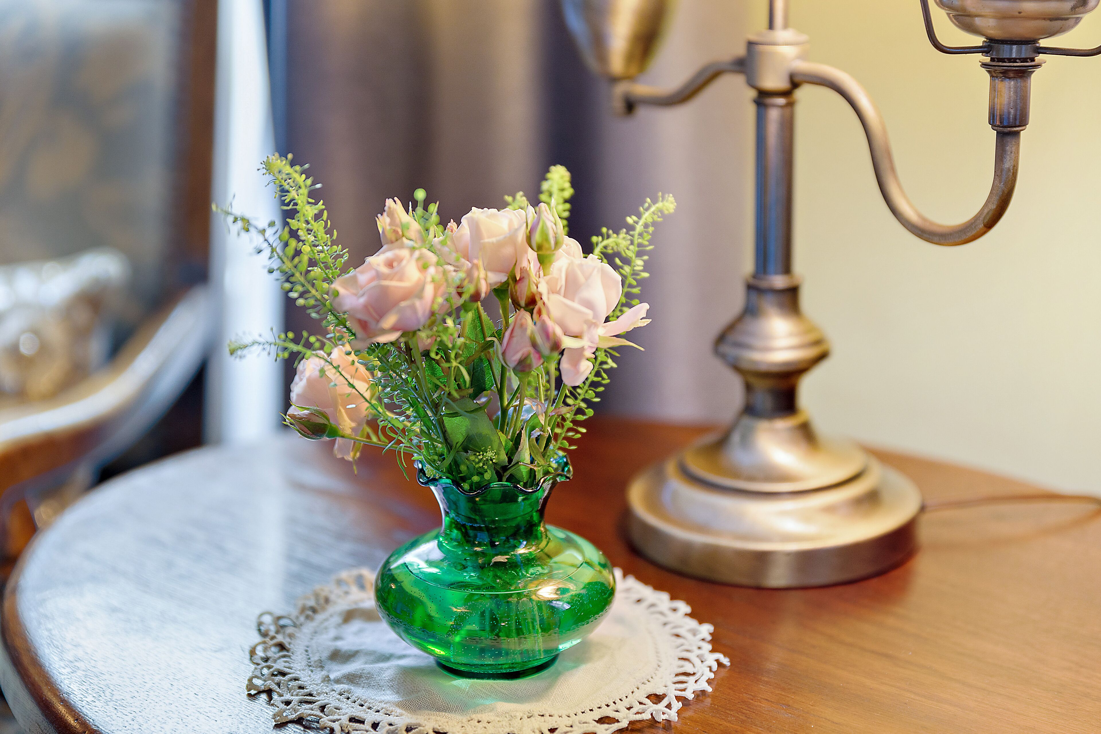Een groene glazen vaas met roze bloemen op een houten tafel met een kantbeschermer.