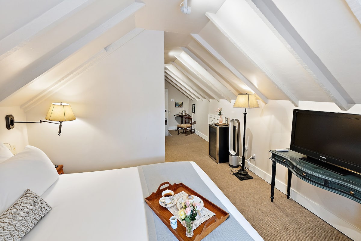 A hotel room with a bed, a tray with breakfast items, a TV, and a desk with a lamp.