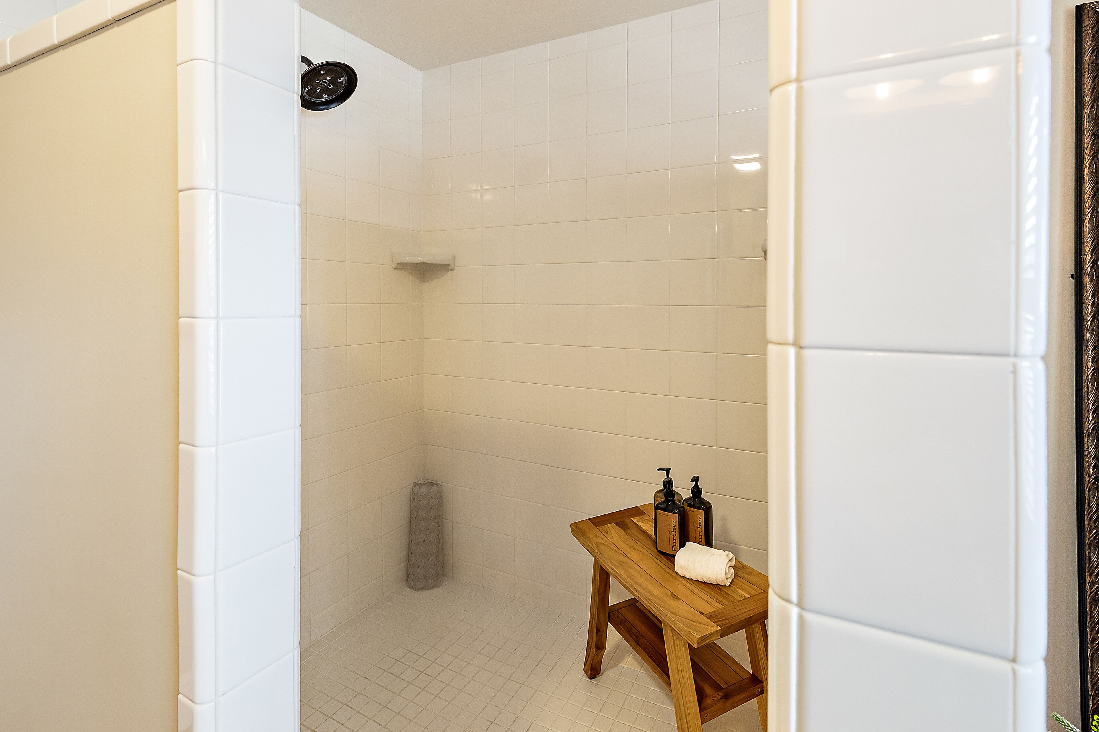 Un baño con azulejos blancos, un banco de madera y dos botellas de champú.