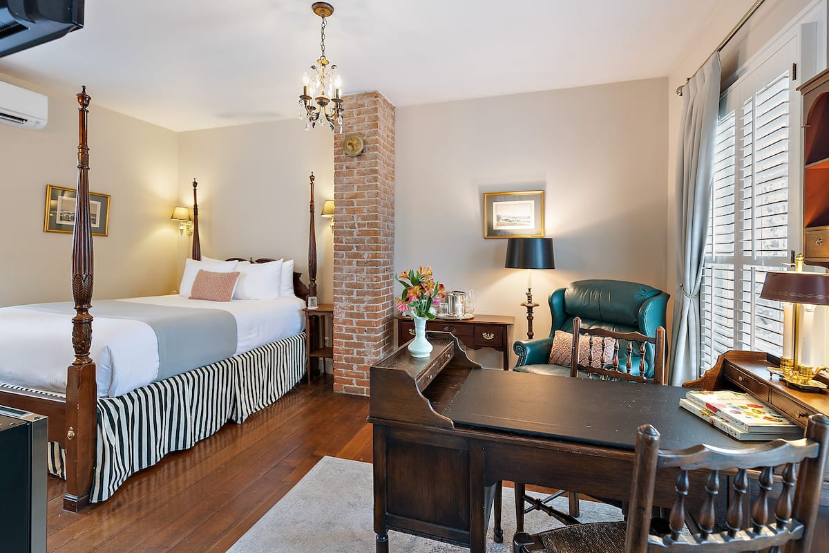 A hotel room with a four-poster bed, a dining table, and a brick accent wall.