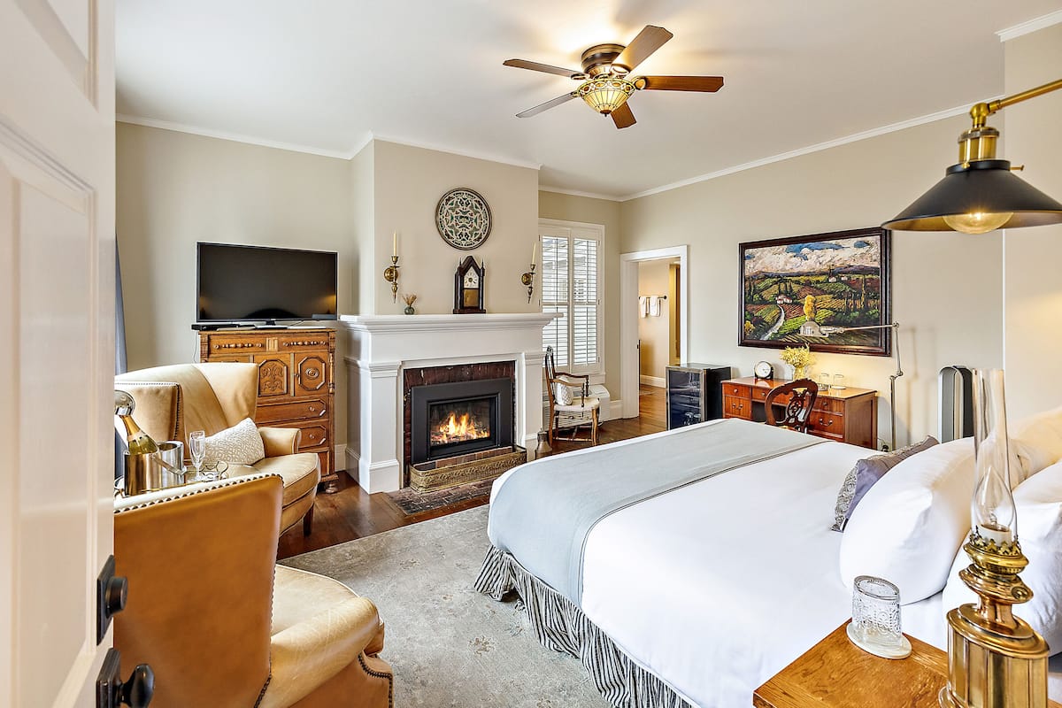 A spacious bedroom with a large bed, a fireplace, a television, and a ceiling fan.