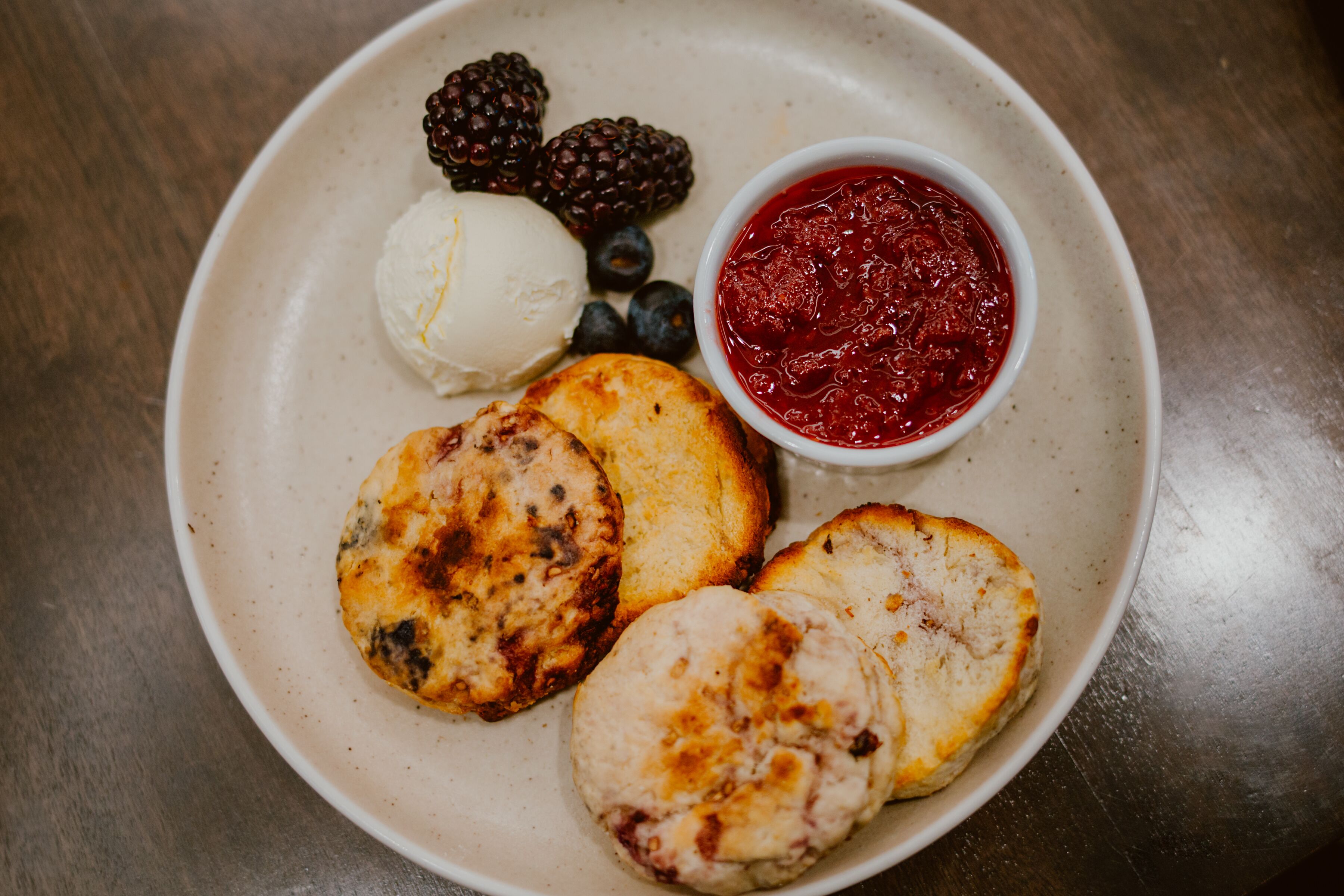 A plate with three scones, a scoop of ice cream, and a bowl of jam.