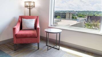 A red armchair with a patterned pillow, a small round table, and a view of a cityscape through a window.