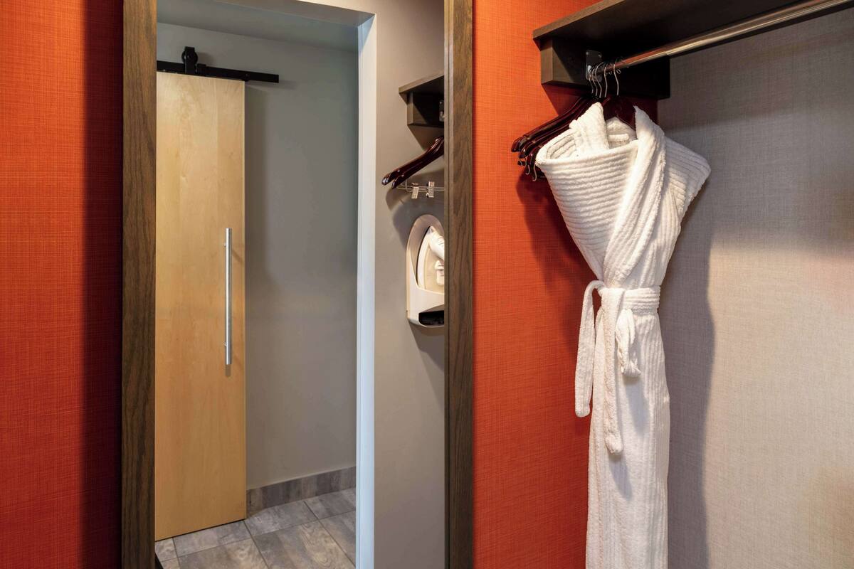 Une salle de bain d’hôtel avec une porte en bois, un porte-serviettes sur lequel est posée une serviette blanche, et une petite étagère contenant des articles de toilette.