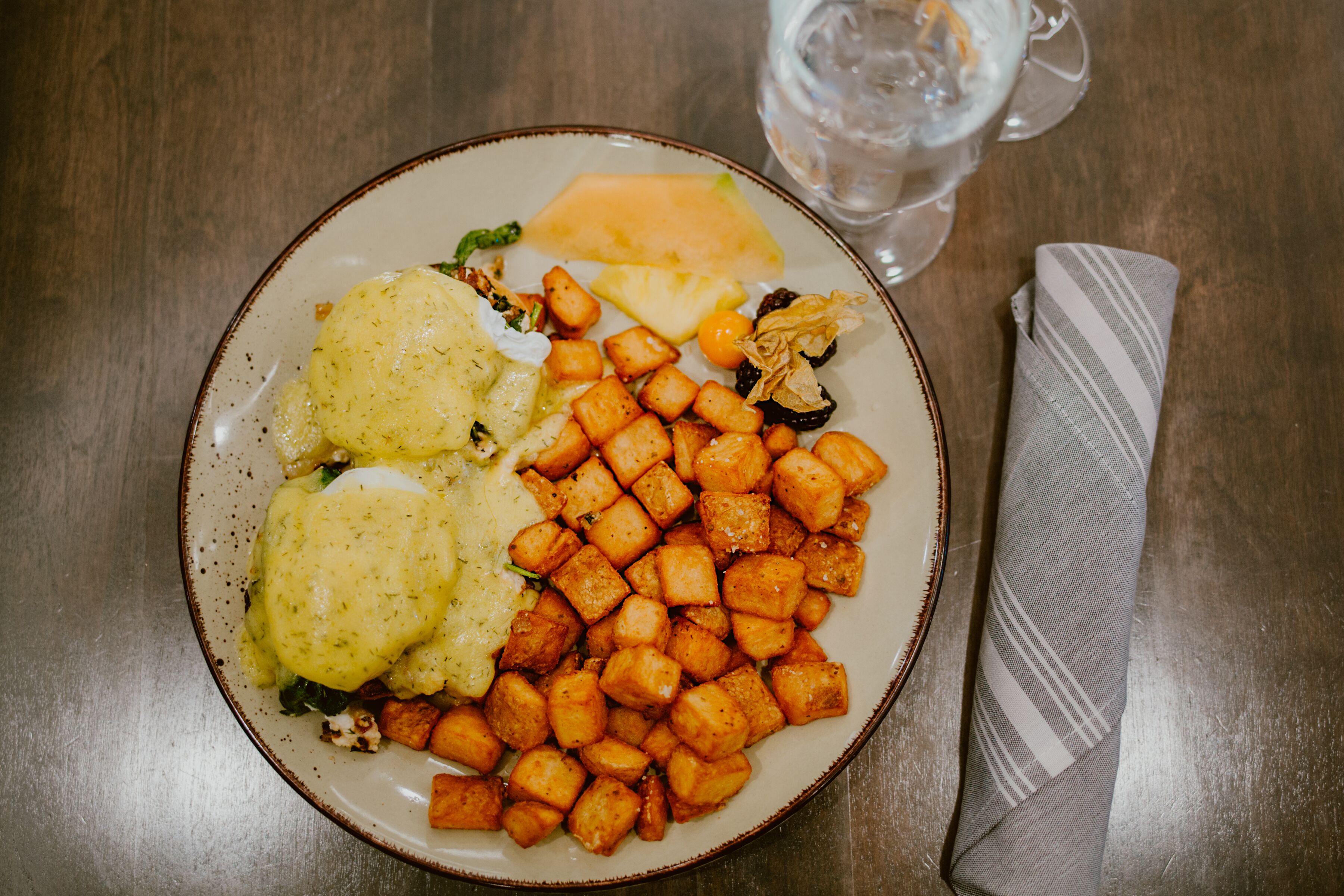 Une assiette de nourriture contenant des pommes de terre et des légumes verts, un verre d’eau et une serviette sur une table en bois.