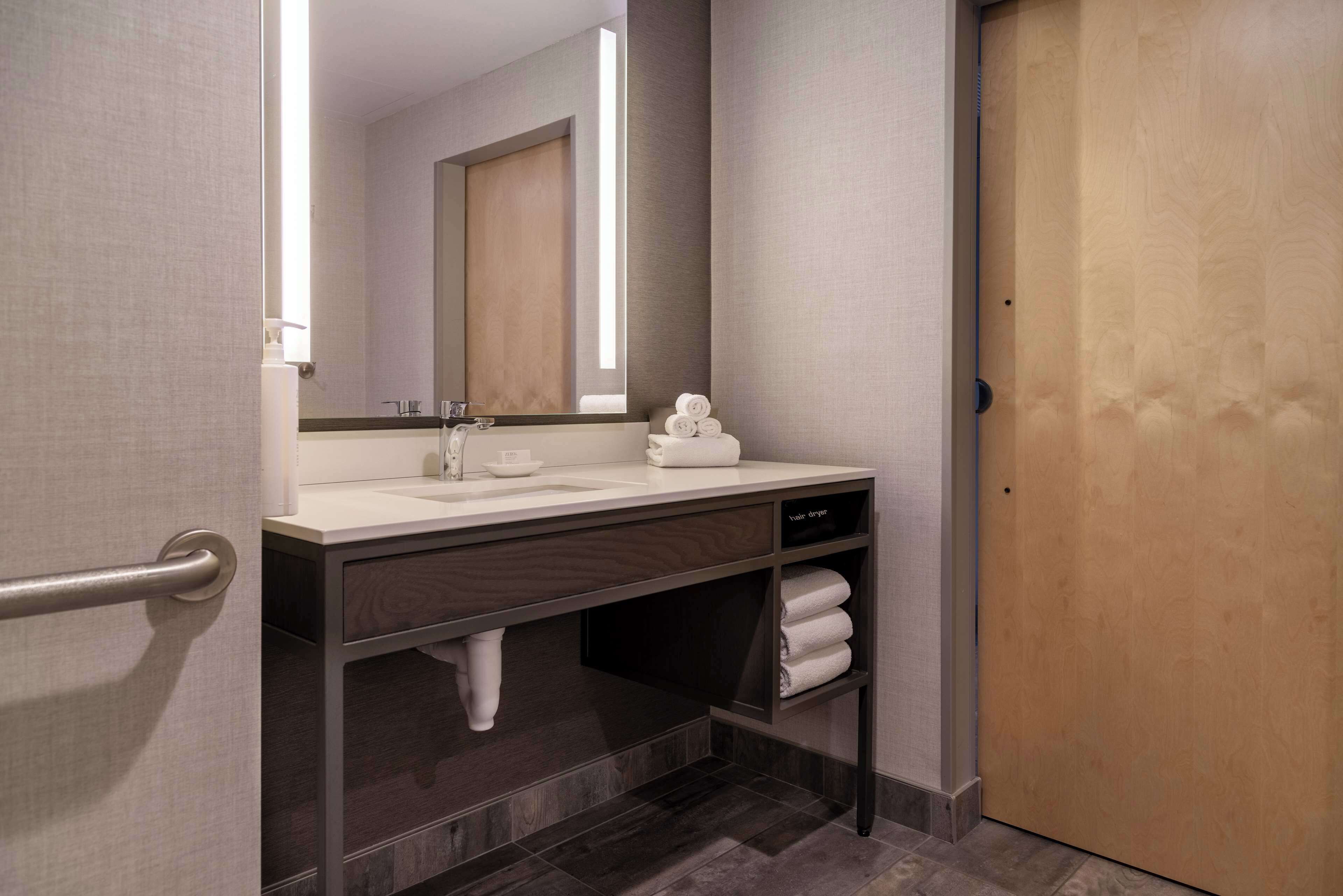A modern bathroom with a sink, mirror, towel rack, and a wooden door.