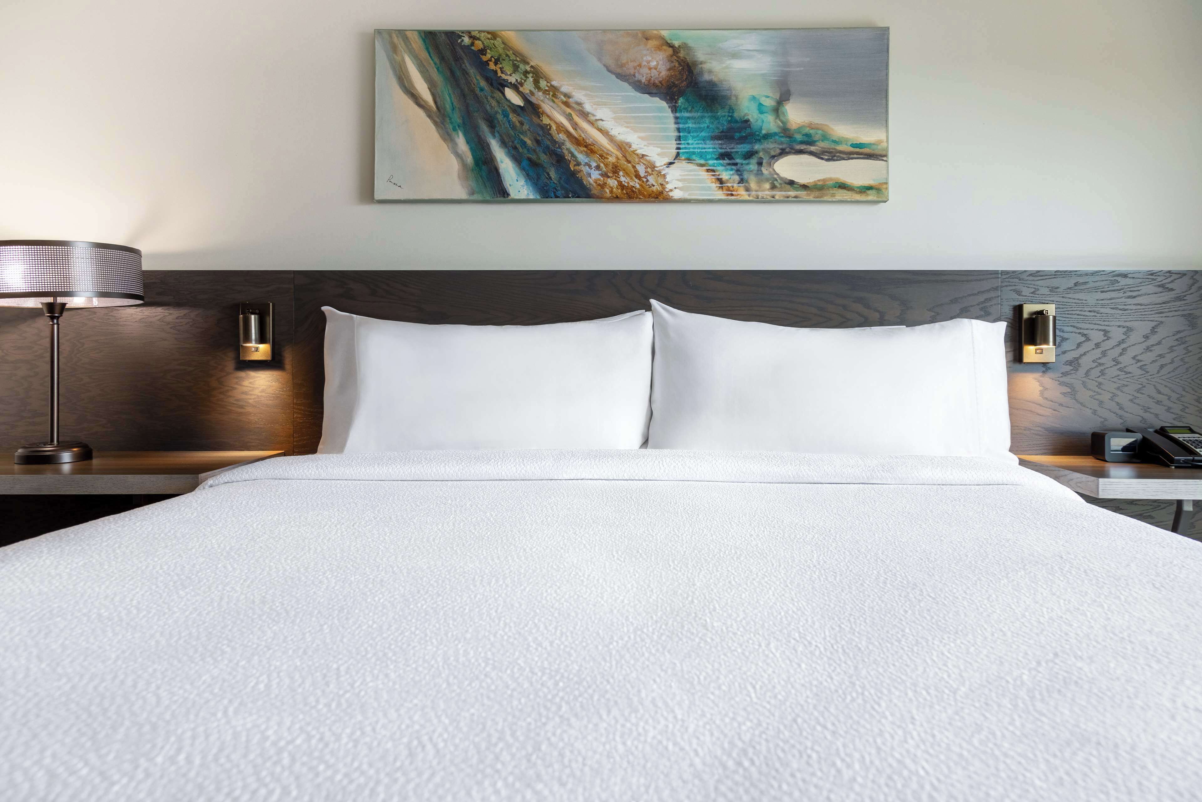 Un lit bien fait, avec du linge de lit blanc, une tête de lit moderne et un tableau accroché au-dessus.