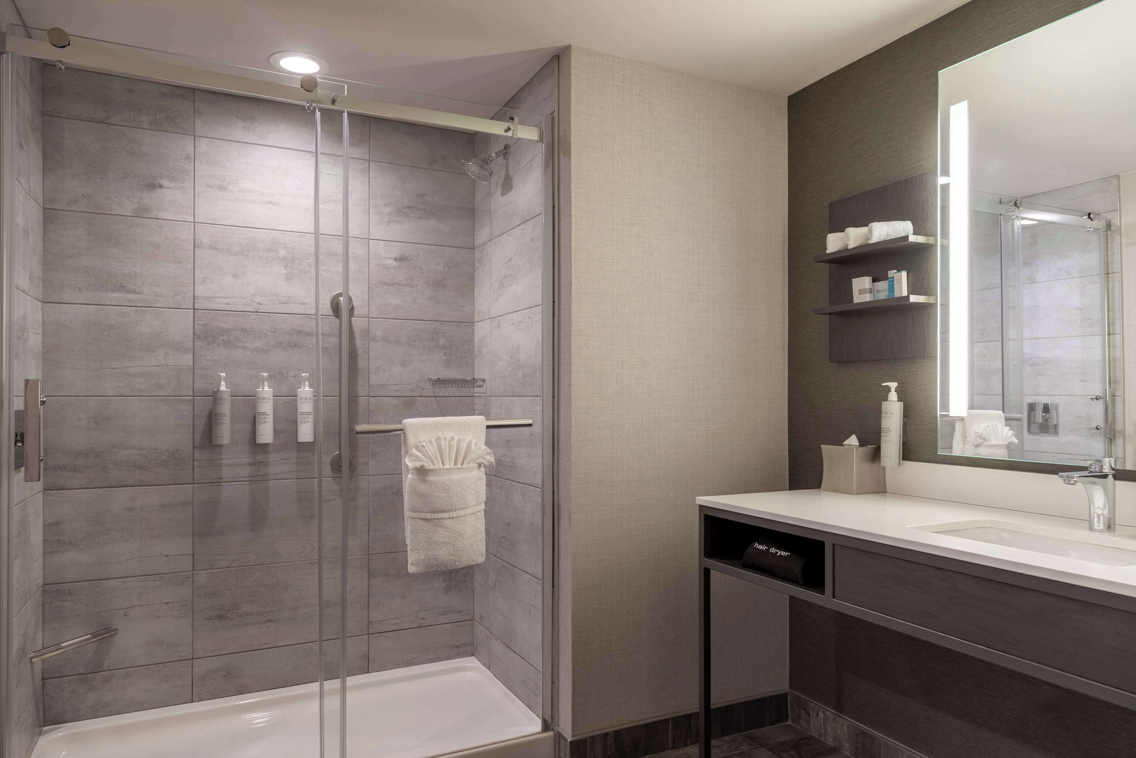A modern bathroom with a glass-enclosed shower, a white sink, and a large mirror.