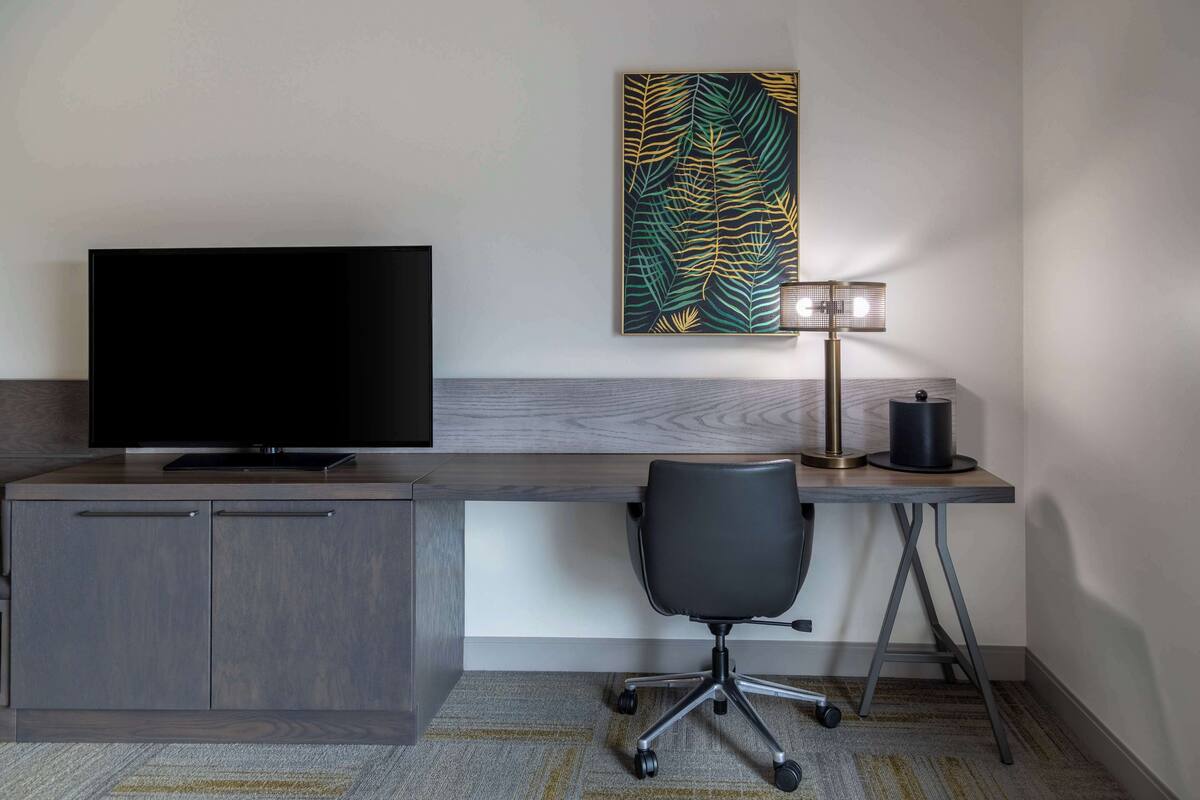 Une chambre d’hôtel moderne équipée d’une télévision à écran plat, d’un bureau avec une lampe et d’une chaise.