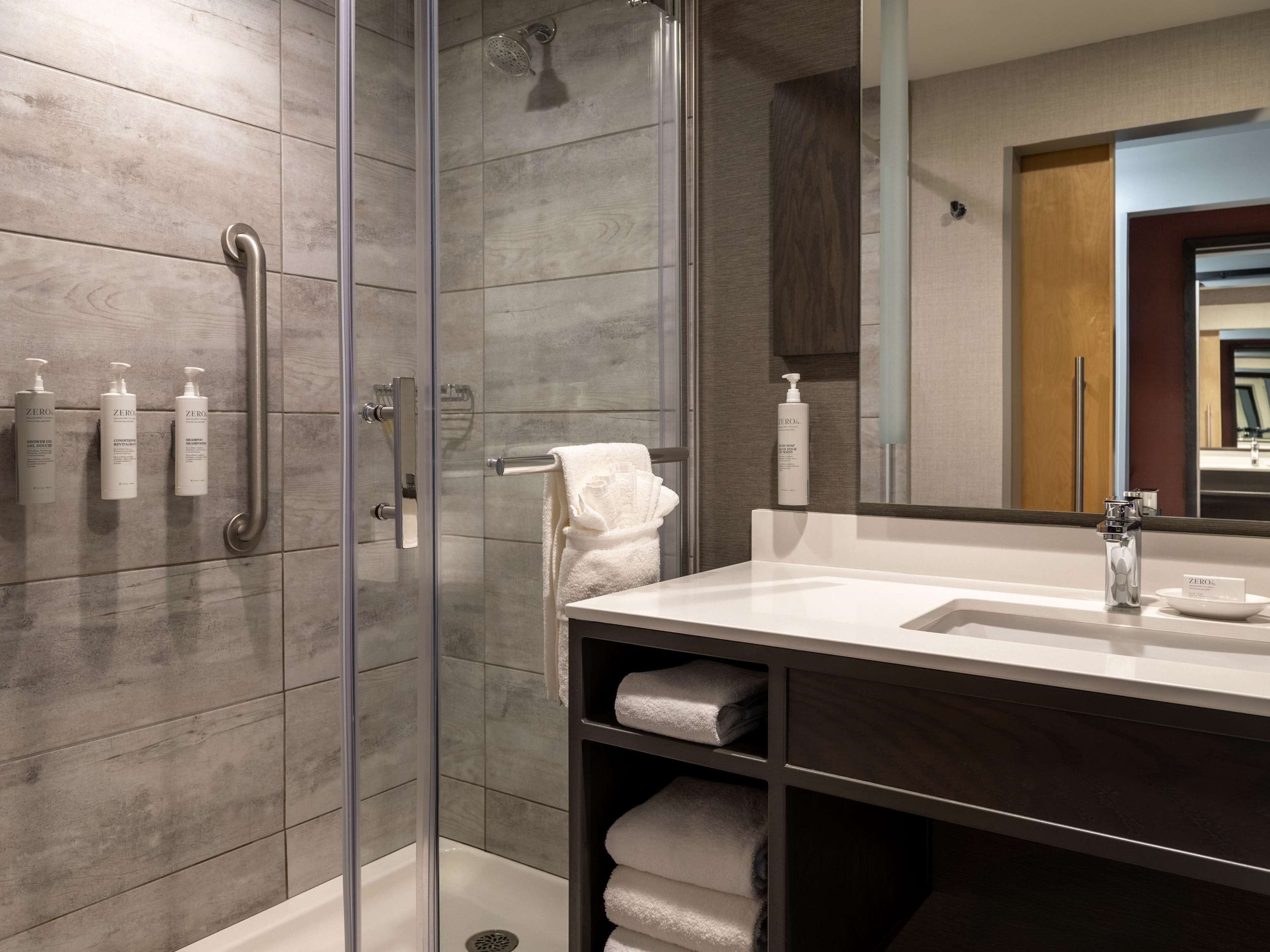 Une salle de bain moderne avec une douche à parois de verre, un meuble-lavabo avec un miroir et un porte-serviettes.
