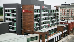Un moderno edificio de hotel con un llamativo letrero de Hilton Garden Inn, varios pisos y una terraza en la azotea.
