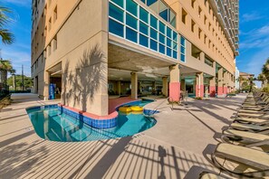 Ein Hotel mit Schwimmbad, Liegestühlen und einem mehrstöckigen Gebäude mit großen Fenstern.