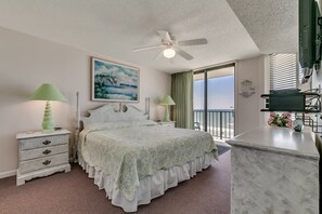 A bedroom with a bed, nightstands, a ceiling fan, a painting, a balcony, and a TV.