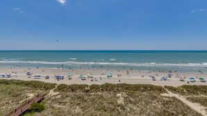 Ein Strand mit einer Holzpromenade, die zum Ufer führt, feinem Sand und Sonnenschirmen.