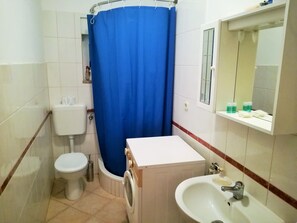Ein kleines Badezimmer mit Toilette, Waschmaschine, Waschbecken und einem blauen Duschvorhang.