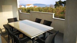 Un balcon avec une table et des chaises, donnant sur une étendue d’eau et des bâtiments.