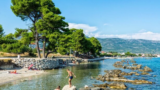 Un paysage côtier avec une plage rocheuse, une eau d’un bleu limpide et, en arrière-plan, des montagnes.