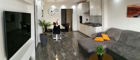 A modern living room with a grey sofa, a coffee table, and a dining area with a table and chairs.