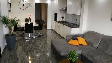 A modern living room with a grey sofa, a coffee table, and a dining area with a table and chairs.