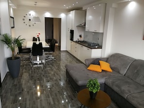 Ein modernes Wohnzimmer mit einem grauen Sofa, einem Couchtisch und einem Essbereich mit Tisch und Stühlen.
