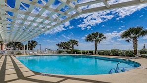 A swimming pool with a clear blue sky, palm trees, and a white pergola structure. - Blue Water Keyes by Condo-World (North Myrtle Beach)