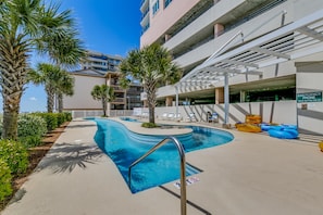 A swimming pool area with palm trees, lounge chairs, and a sign for an emergency phone. - Blue Water Keyes by Condo-World (North Myrtle Beach)