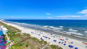 A beach with a boardwalk, beach umbrellas, and a building with a colorful exterior. - Blue Water Keyes by Condo-World (North Myrtle Beach)