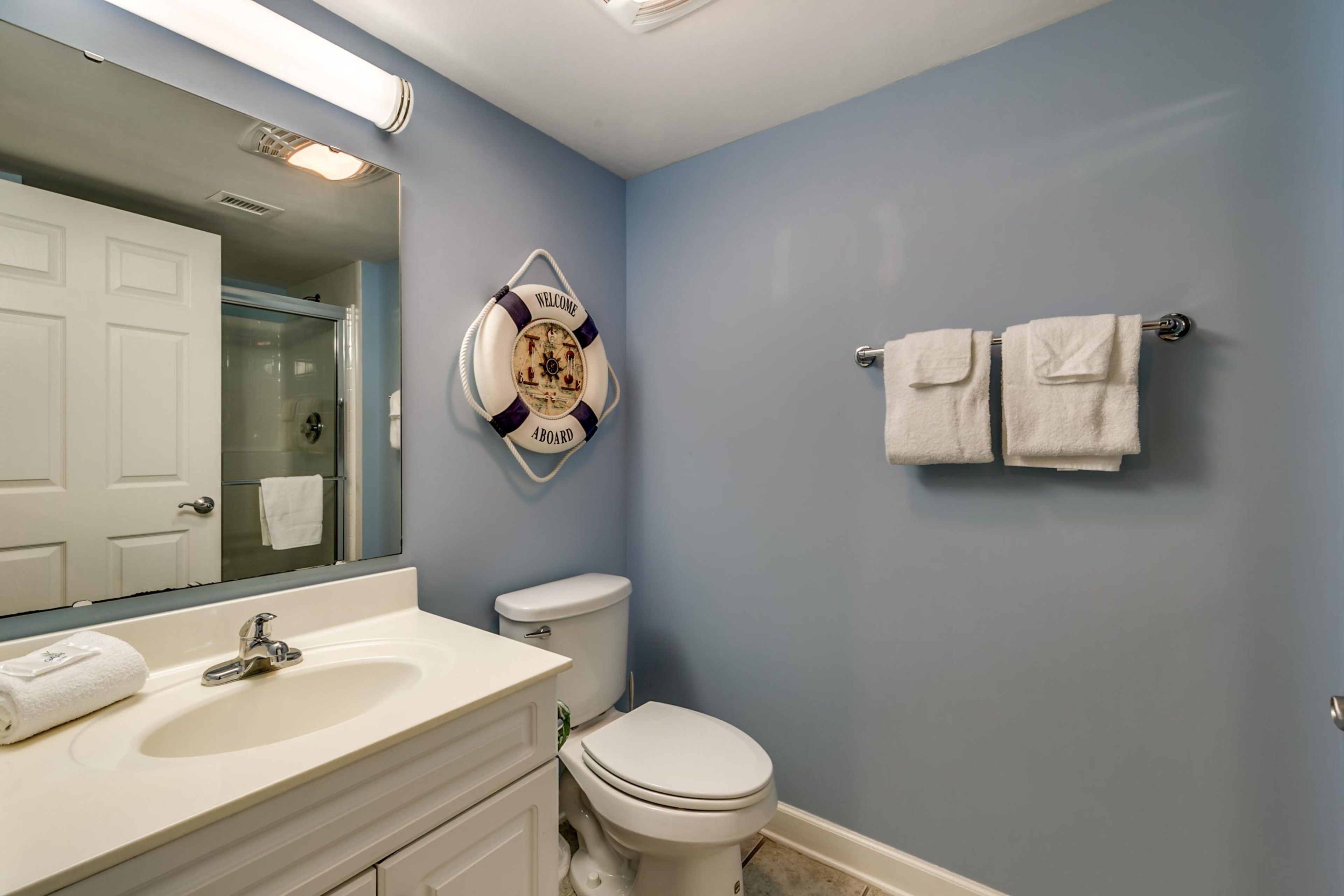 Une salle de bain avec un lavabo blanc, des toilettes, un grand miroir et un gilet de sauvetage accroché au mur.