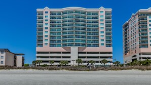 A multi-story hotel with a curved facade, multiple balconies, and a parking structure at the base. - Blue Water Keyes by Condo-World (North Myrtle Beach)