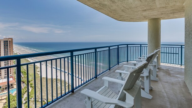 Ein Balkon mit weißen Stühlen mit Blick auf Strand und Meer.