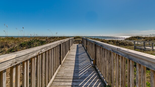 Une promenade en bois qui mène à une plage, sous un ciel dégagé.