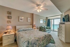 A bedroom with a bed, nightstands, a dresser, a ceiling fan, and a view of the ocean through large windows. - Crescent Keyes by Condo-World (North Myrtle Beach)