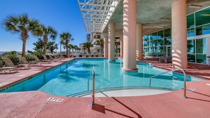 A pool area with lounge chairs, palm trees, and a view of a building with large windows.