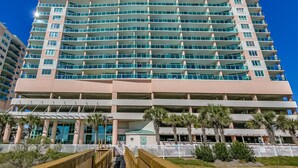 A multi-story hotel with a modern design, featuring balconies, a central atrium, and a white fence surrounding the property.