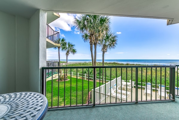 Ein Balkon mit Blick auf das Meer, Palmen und eine Rasenfläche mit Gartenmöbeln.
