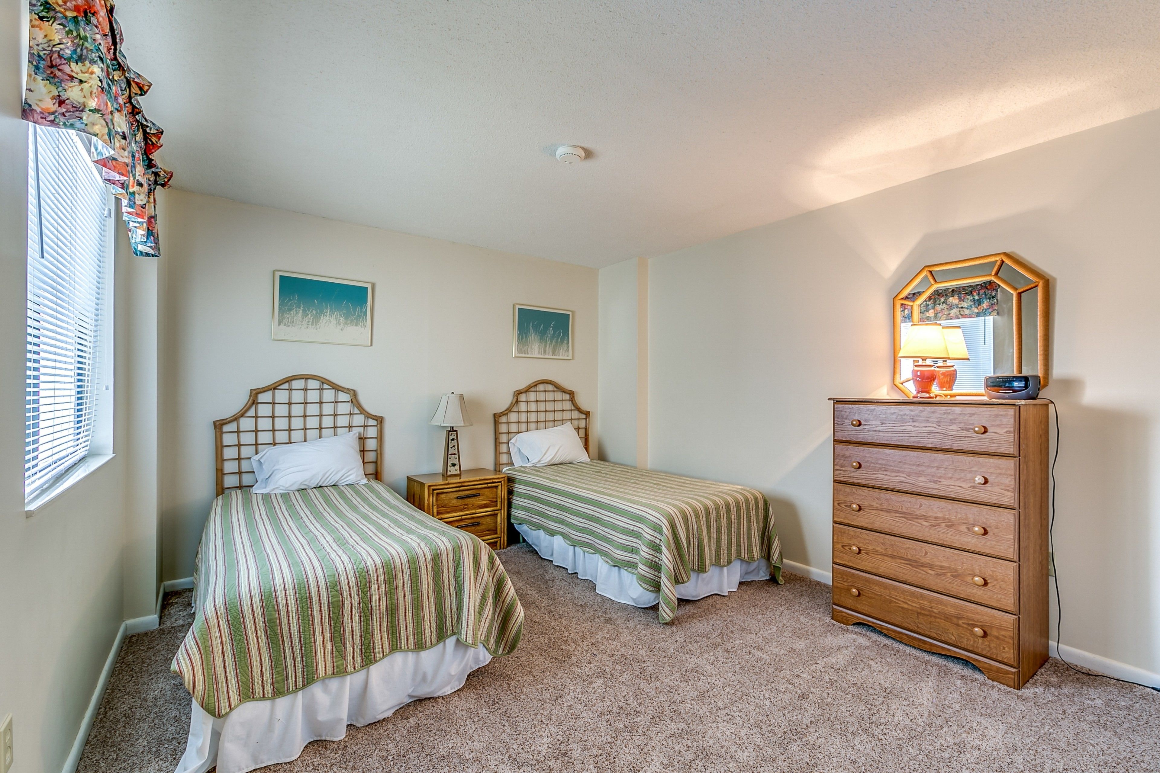 A bedroom with two single beds, a wooden dresser, and a mirror.