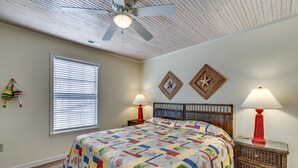 A bedroom with a bed, two nightstands, a ceiling fan, a window with blinds, and wall decorations. - High C's by Condo-World (North Myrtle Beach)