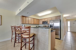A kitchen with wooden cabinets, a stainless steel refrigerator, a microwave, and a bar area with chairs.