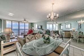 Een ruime woonkamer met een glazen tafel, witte stoelen, een rode stoel en een bank.