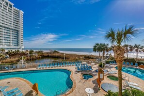 A hotel pool area with multiple pools, sun loungers, and a view of the ocean. - Sea Watch Resort by Condo-World (Myrtle Beach)