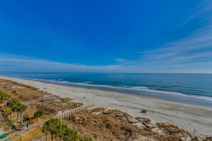 A beach with a wooden walkway leading to a sandy area, a clear blue sky, and the ocean in the background.