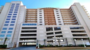 Un hotel de varios pisos con un atrio central, múltiples balcones y un aparcamiento.