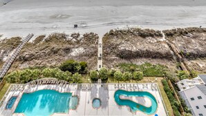 Zona de piscina con varias piscinas, un muelle de madera y vistas a la playa.