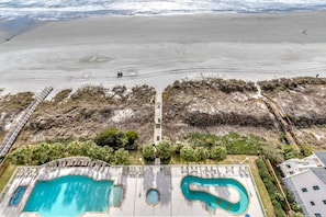 A pool area with multiple pools, a wooden deck, and a view of the beach.