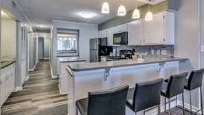 A modern kitchen with a central island, bar stools, stainless steel appliances, and pendant lighting. - Summit by Condo-World (North Myrtle Beach)