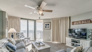 A living room with a large TV, a ceiling fan, and a view of the ocean. - Summit by Condo-World (North Myrtle Beach)