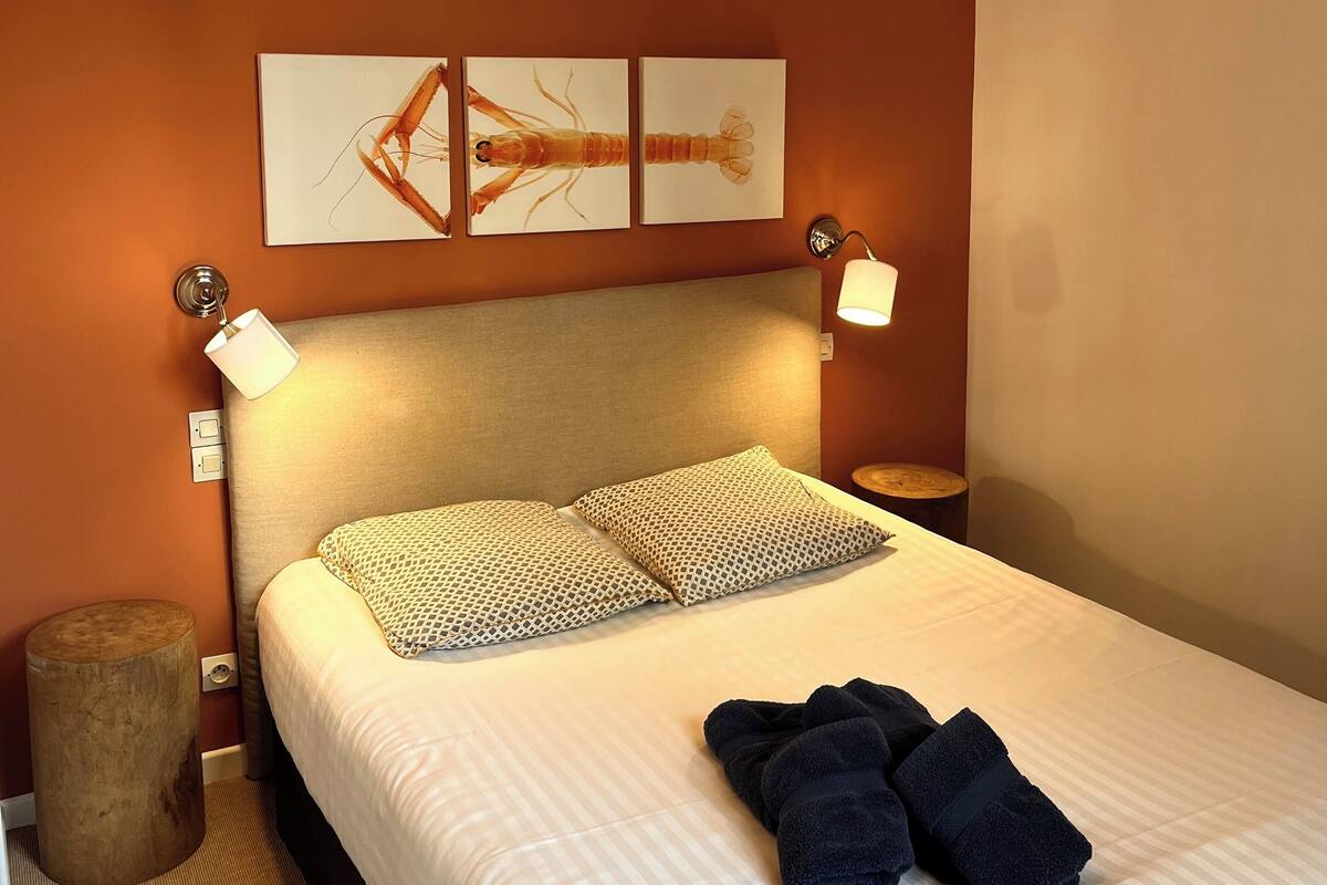 A neatly made bed with patterned pillows, a headboard, and a wall-mounted artwork of a shrimp.