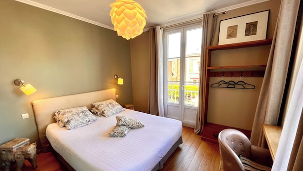 A neatly made bed with patterned pillows, a hanging light fixture, a chair, and a door leading to an outdoor balcony. - Hotel d'Angleterre (Etretat)
